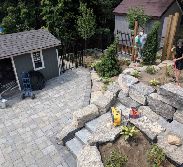 JD Landscape Design team installing an interlock paver patio and natural stone retaining wall in a residential backyard in Waterloo, Ontario — professional outdoor construction and landscaping craftsmanship