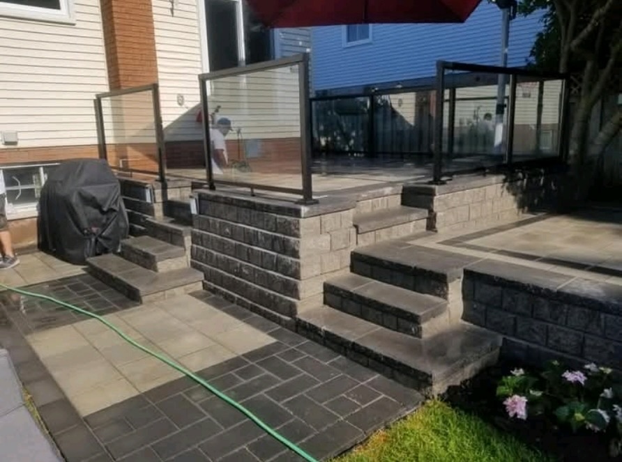 Interlock patio with natural stone steps, retaining walls, and glass railing installed by JD Landscape Design — residential outdoor construction project in Waterloo, Ontario